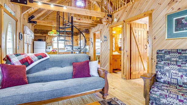 A cozy cabin interior with a wooden ceiling, a sofa with a blanket, and a patterned chair. - Quaint Dahlonega Cabin w/ Cavenders Creek Access! (Dahlonega)
