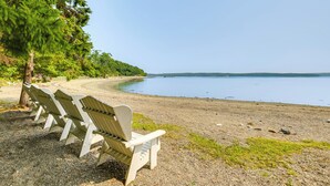 A row of Adirondack chairs on a pebble beach with a calm lake and a forested area in the background. - ‘The Beachhouse’ Retreat w/ Prescot Bay Views! (Stockton Springs)