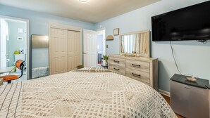 Quarto com cama, cômoda, televisão e geladeira.