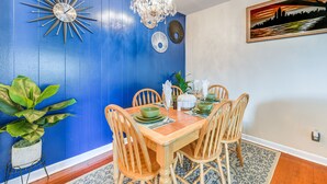 Uma sala de jantar com parede azul, um lustre e um quadro.