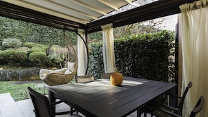 Un porche cubierto con una mesa y sillas, un sillón colgante y una decoración central con una calabaza grande.