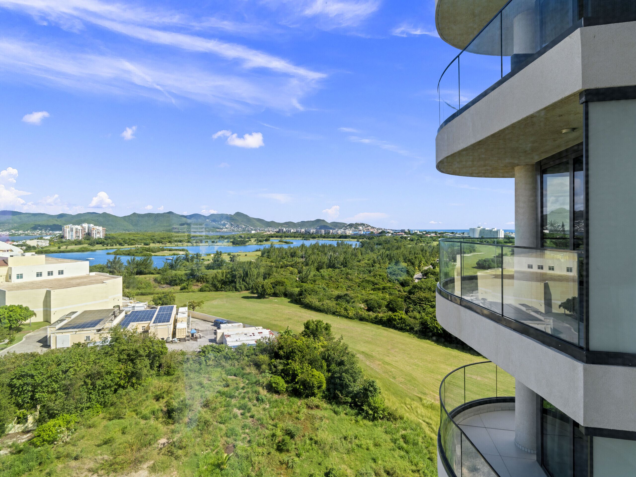 Um edifício moderno com varanda de vidro com vista para um lago e vegetação.