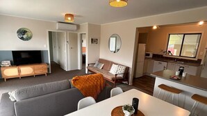 Moderni olohuone, jossa on sohva, ruokapöytä sekä keittiöalue, jossa on jääkaappi ja mikroaaltouuni.