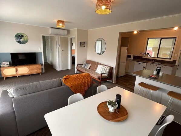 Ein modernes Wohnzimmer mit einer Couch, einem Esstisch und einer Küchenzeile inklusive Kühlschrank und Mikrowelle.