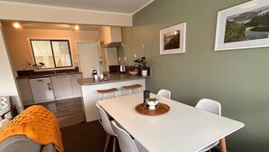 Moderni keittiö, jossa on valkoiset kaapit, keskellä oleva keittiösaareke sekä ruokailutila, jossa on valkoinen pöytä ja tuolit.