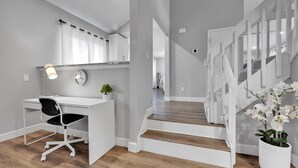 Un intérieur moderne et épuré, aux couleurs claires, comprenant un bureau, une chaise et un escalier.