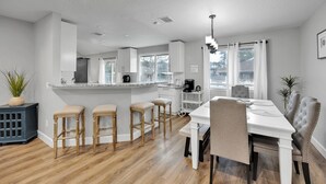 Une cuisine moderne dotée d’un îlot central, de tabourets de bar et d’un coin repas avec une table et des chaises blanches.