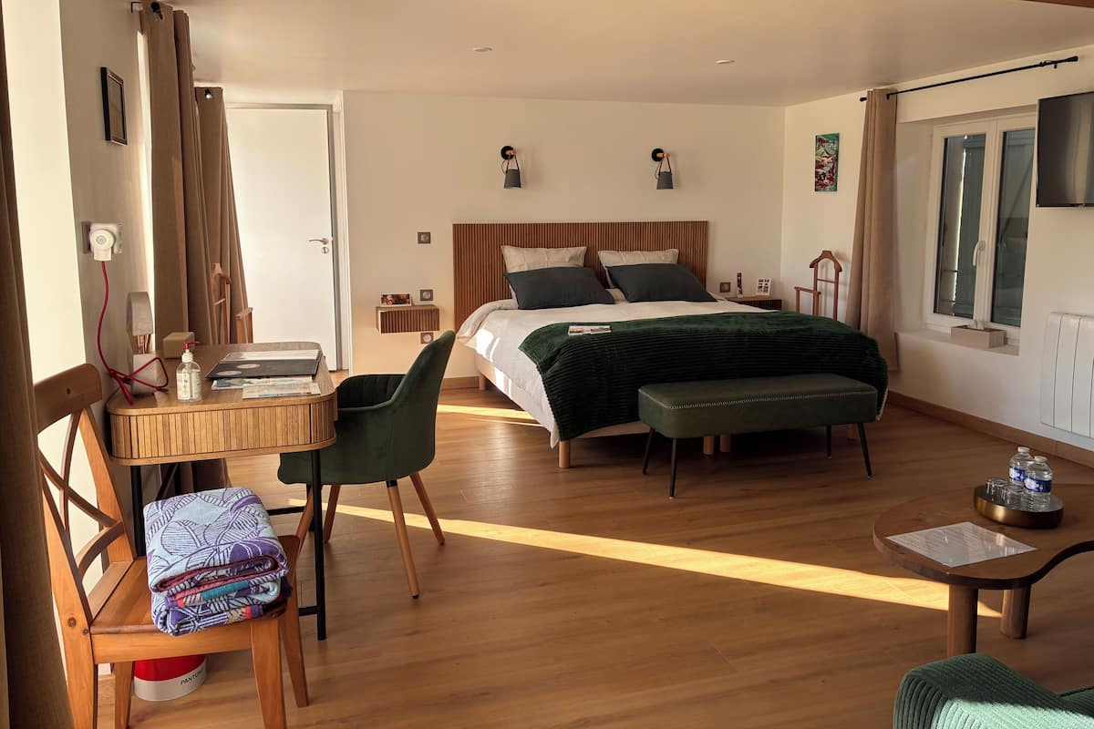 A hotel room with a bed, a desk, a chair, a bench, and a window.