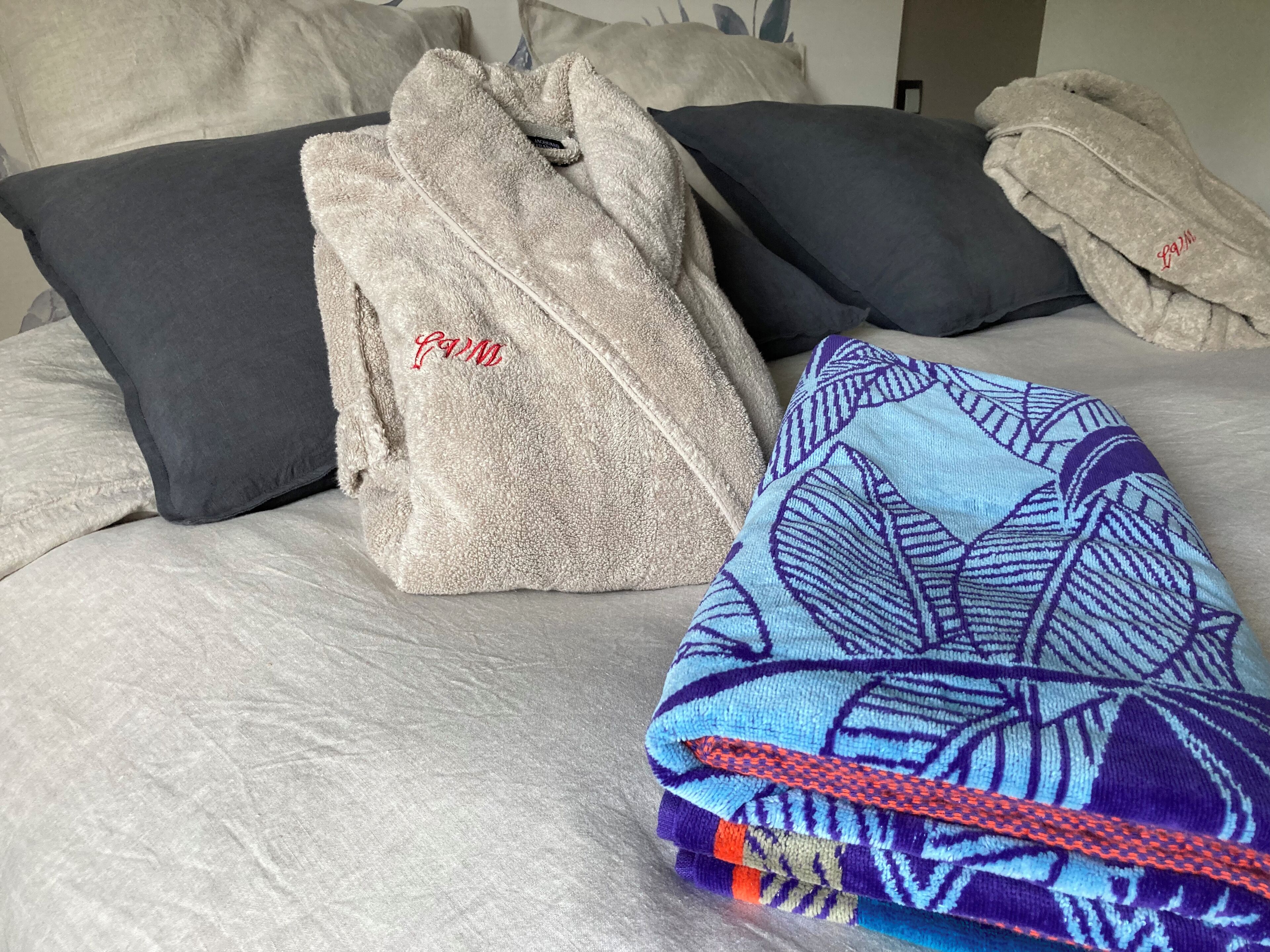 Ein Bett mit grauer Decke, blumigem, blauem Überwurf und drei Kissen in Grau und Schwarz.