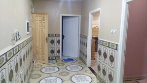 A hallway with patterned tiles, a wooden door, and a blue mat on the floor.