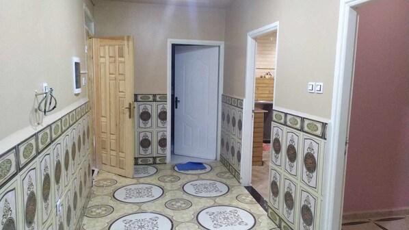 A hallway with patterned tiles, a wooden door, and a blue mat on the floor.