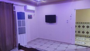 A room with a bed, an air conditioner, a flat-screen TV mounted on the wall, and a patterned tile floor.