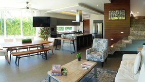 Een moderne keuken met een groot eiland, een eetgedeelte met een houten tafel en bankjes, een fauteuil met een patroon en een trap met een marmeren afwerking.