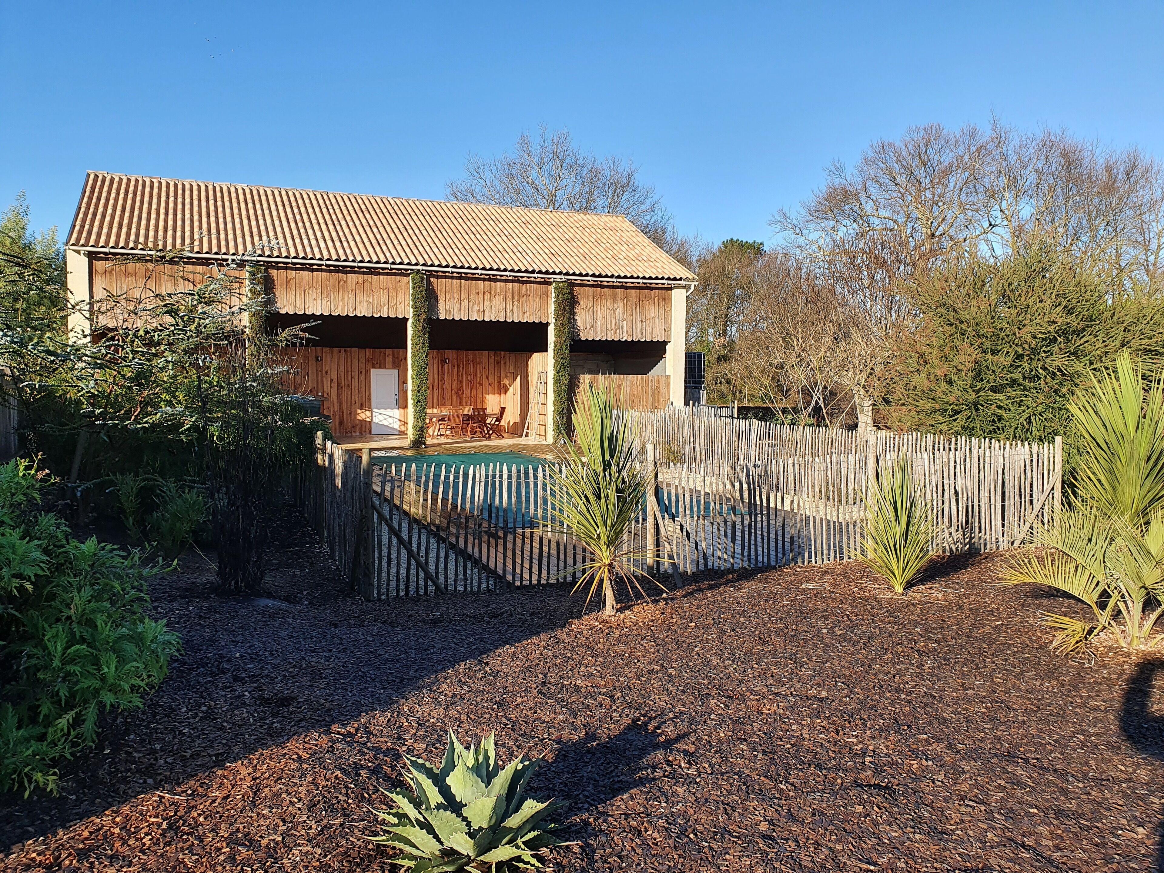 A wooden house with a thatched roof, a wooden deck, and a pool.