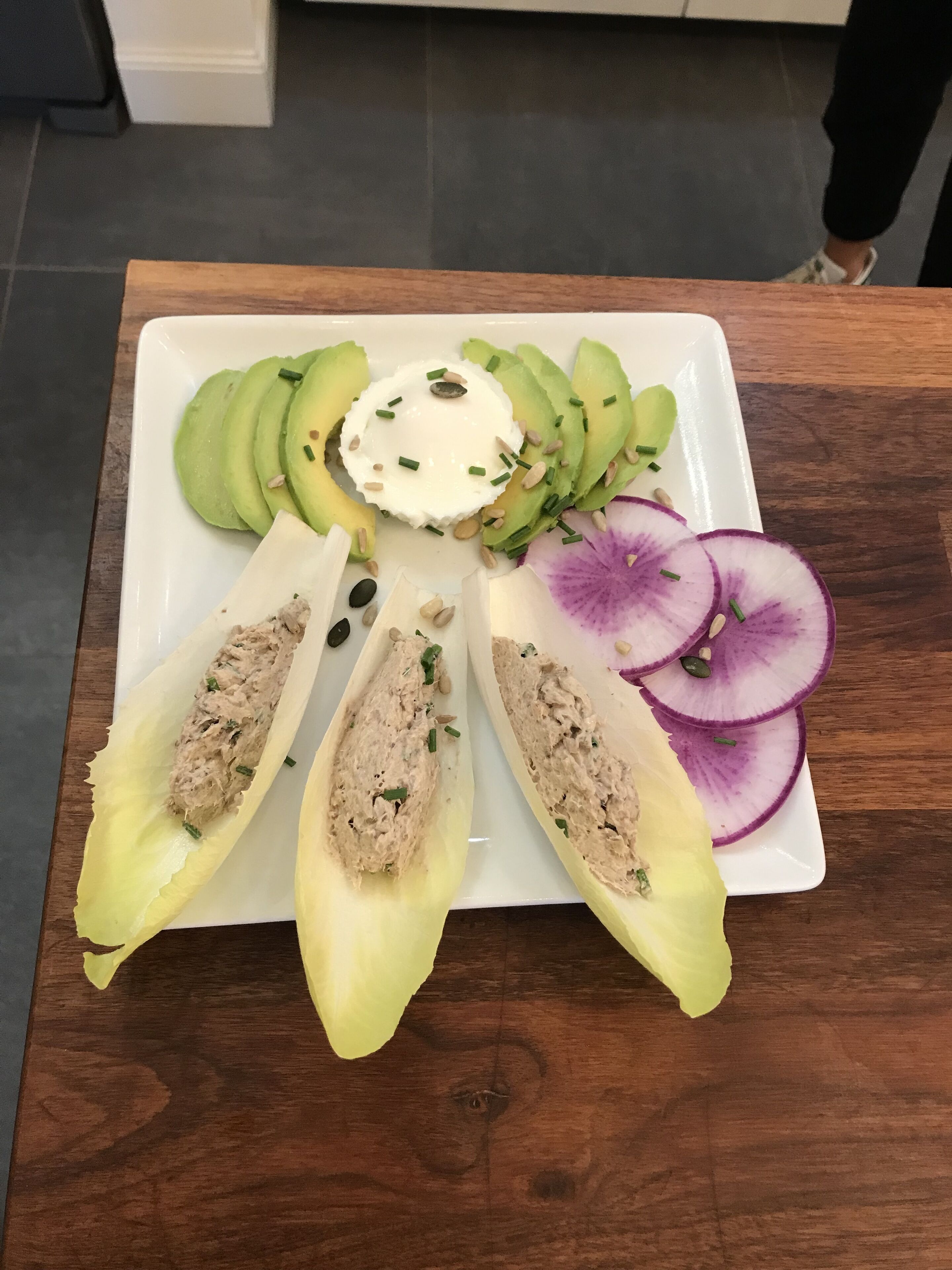 Un plato blanco con una variedad de alimentos, entre ellos aguacate en rodajas, una cucharada de crema y un aderezo en una hoja de lechuga hendida.