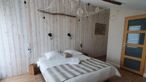 A bedroom with a wooden wall, a bed with white bedding, a striped blanket, and a wooden floor. - VILLA L'ESTUAIRE (Braud-et-Saint-Louis)