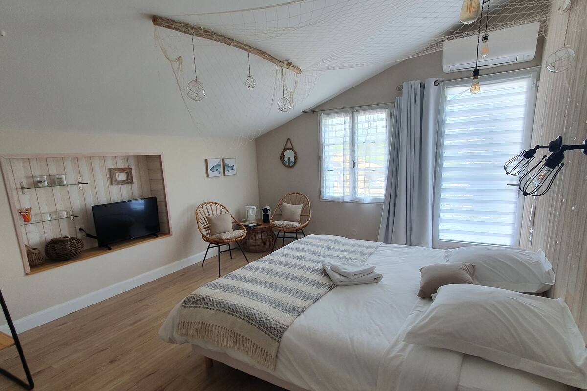 A bedroom with a bed, a TV, a seating area with chairs, and a window with curtains.