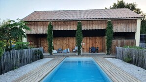 A wooden deck with a rectangular pool, surrounded by a wooden fence and a wooden building with a tiled roof. - VILLA L'ESTUAIRE (Braud-et-Saint-Louis)