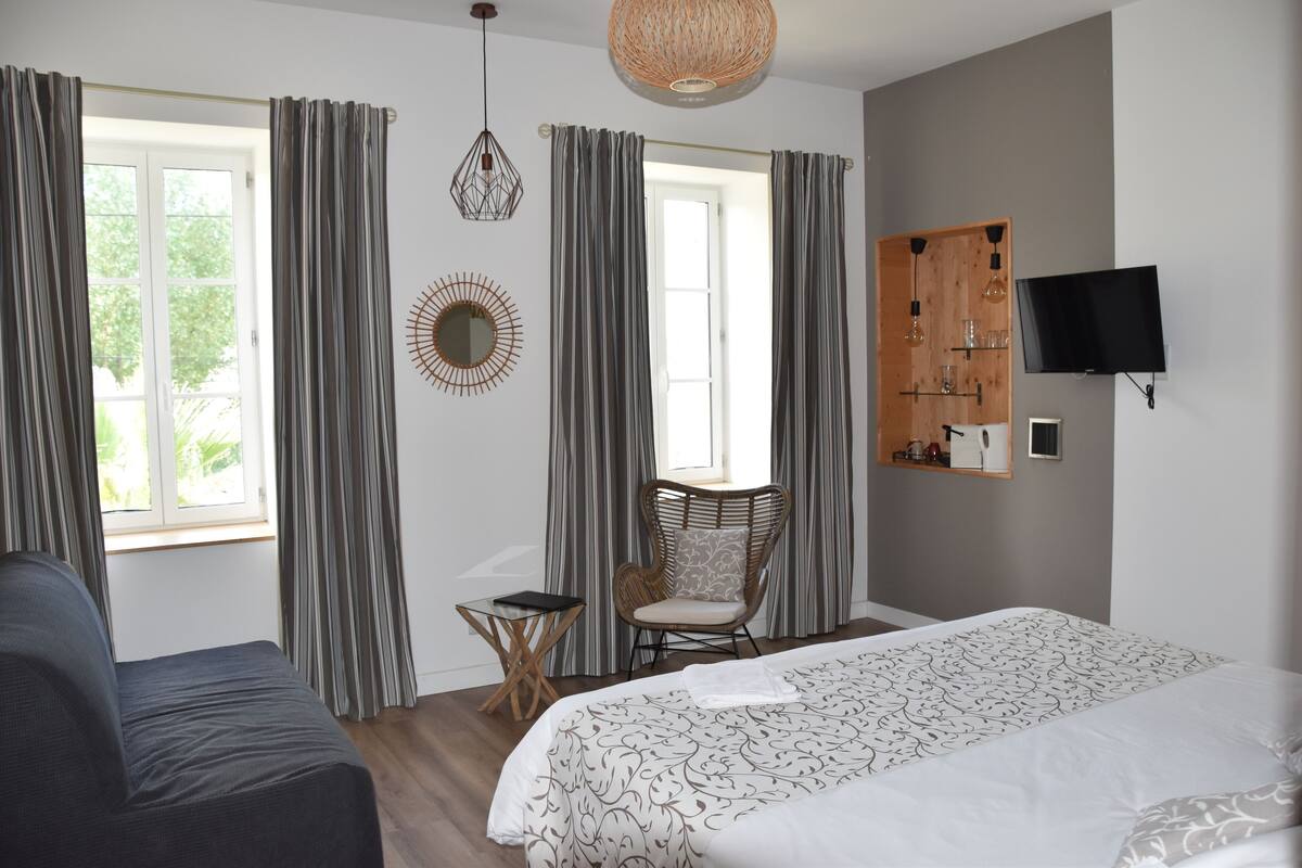 A bedroom with a large bed, a chair, a small table, and a TV on the wall.