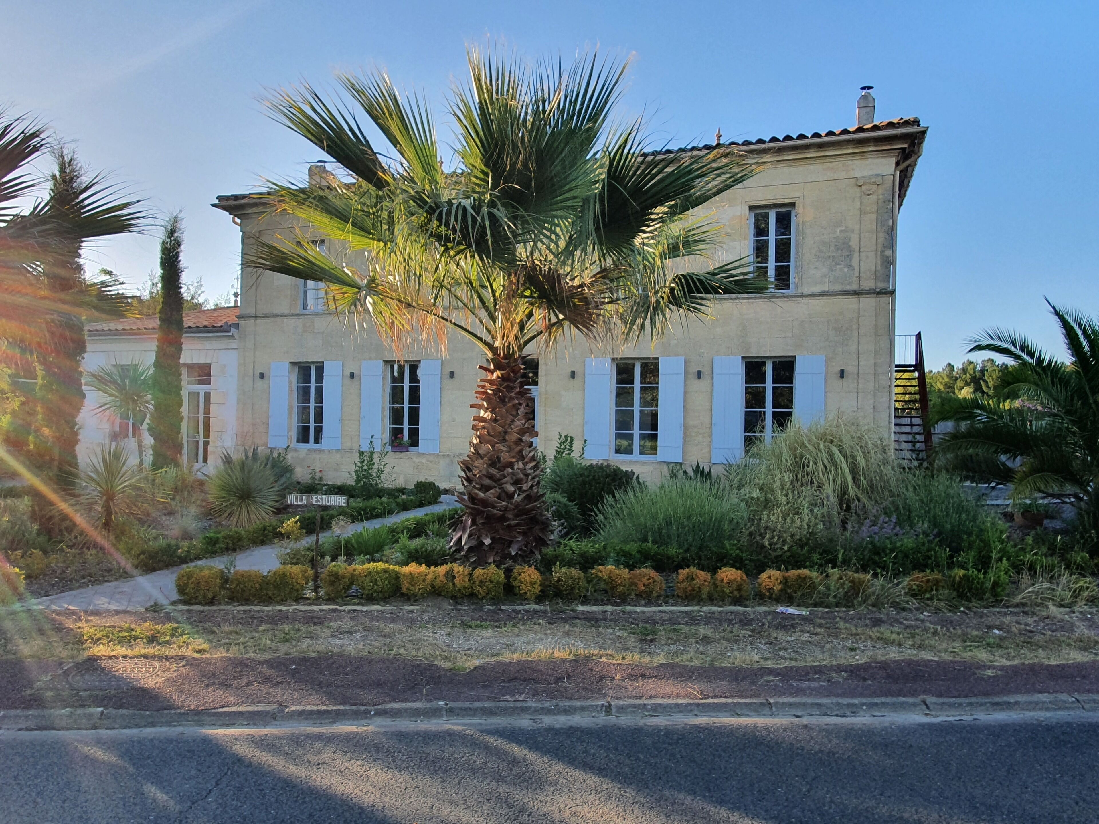 Un edificio de dos pisos con fachada simétrica, una entrada central y un jardín bien cuidado con una palmera.
