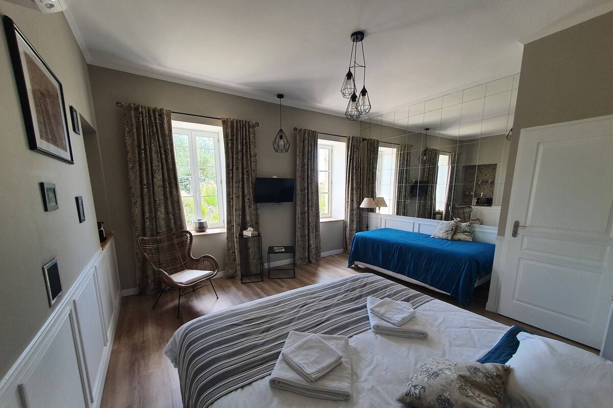 A hotel room with a large bed, a smaller bed, a chair, a television, and a window with curtains.