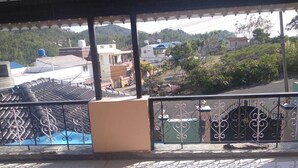 Un balcon doté d’une rambarde en métal, d’un sol carrelé et offrant une vue sur un quartier résidentiel avec des maisons et des arbres.