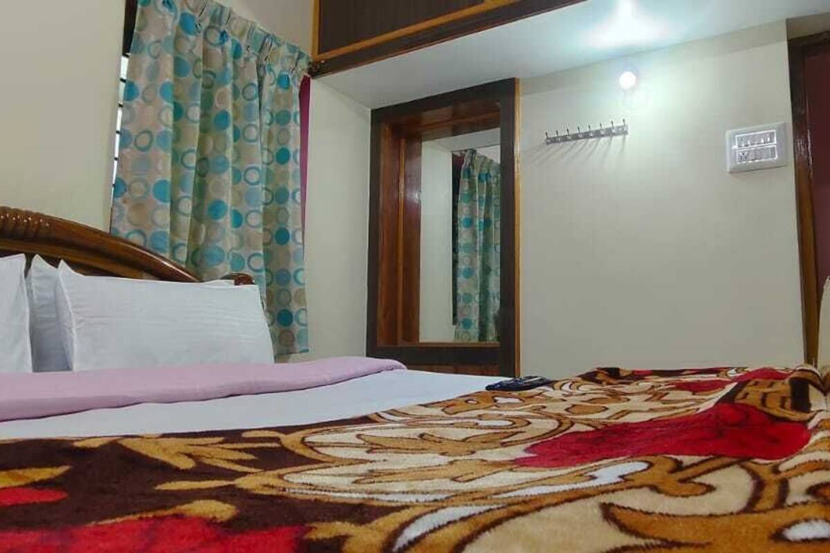 Quarto de hotel com cama, espelho, porta e luminária fixada na parede.