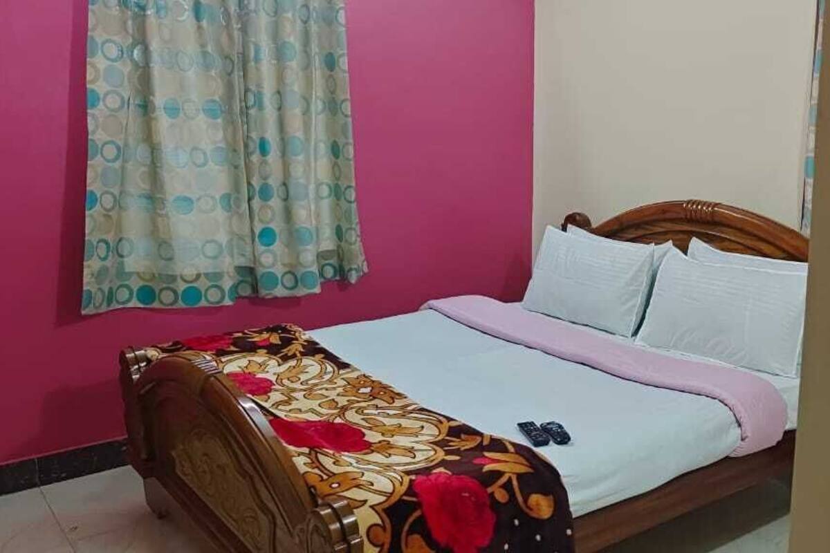 Quarto com cama, cabeceira de madeira, parede rosa e cortina com padrão de bolinhas.