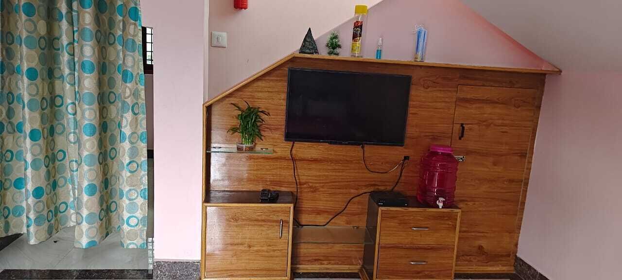 A wooden desk with a flat-screen TV, drawers, a small plant, and a water dispenser.