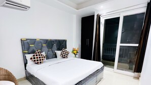 A modern bedroom with a large bed, a headboard with geometric patterns, a wicker chair, and a view through a sliding glass door. - Roomshala 160 Hotel Red (New Delhi)
