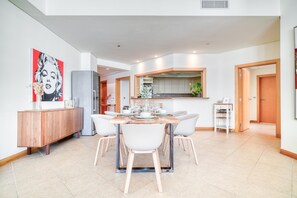 A modern dining area with a central table, white chairs, and a wooden cabinet. - Chic Beachside 3BR Living at the Palm (Dubai)