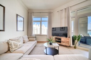 A modern living room with a sofa, TV, and a view of buildings through large windows.