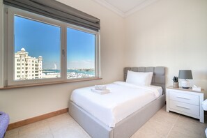 A hotel room with a large bed, a nightstand, and a view of a cityscape through the window.