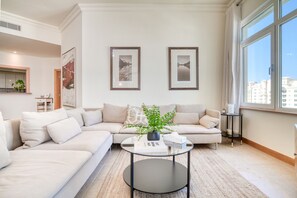 A modern living room with a beige sectional sofa, a glass coffee table, and two framed pictures on the wall.