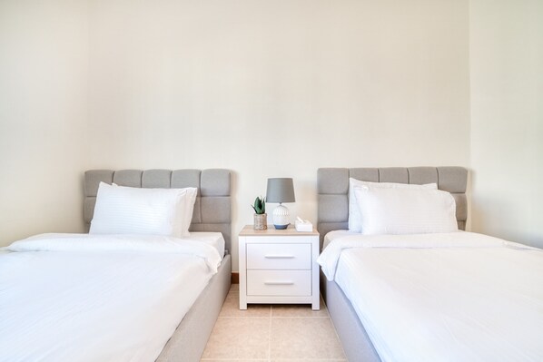 A hotel room with two beds, a nightstand with a lamp, and a small plant.