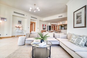 A spacious living room with a modern sofa set, a glass coffee table, and a dining area in the background.
