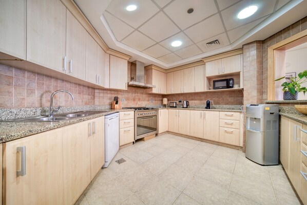 A modern kitchen with light wood cabinets, granite countertops, stainless steel appliances, and a built-in microwave.
