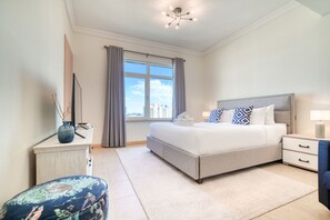 A modern bedroom with a large bed, a nightstand, a dresser, and a window with curtains.