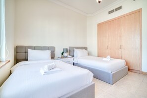A hotel room with two beds, a nightstand, a lamp, a plant, and a wardrobe. - Chic Beachside 3BR Living at the Palm (Dubai)