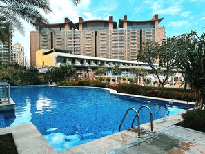 Ein Pool mit modernem Design, umgeben von üppiger Vegetation und einem Hotel im Hintergrund.