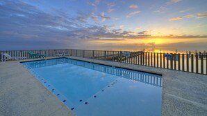 Una piscina rettangolare con bordo in legno e recinzione, circondata da una vista panoramica al tramonto.