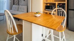 A modern kitchen with a wooden table, white chairs, a microwave, and a refrigerator. - Anahata Home (Tabanan)