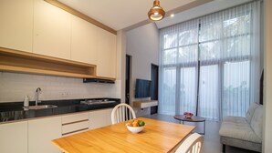 A modern kitchen with white cabinets, a wooden countertop, and a dining area with a wooden table. - Anahata Home (Tabanan)
