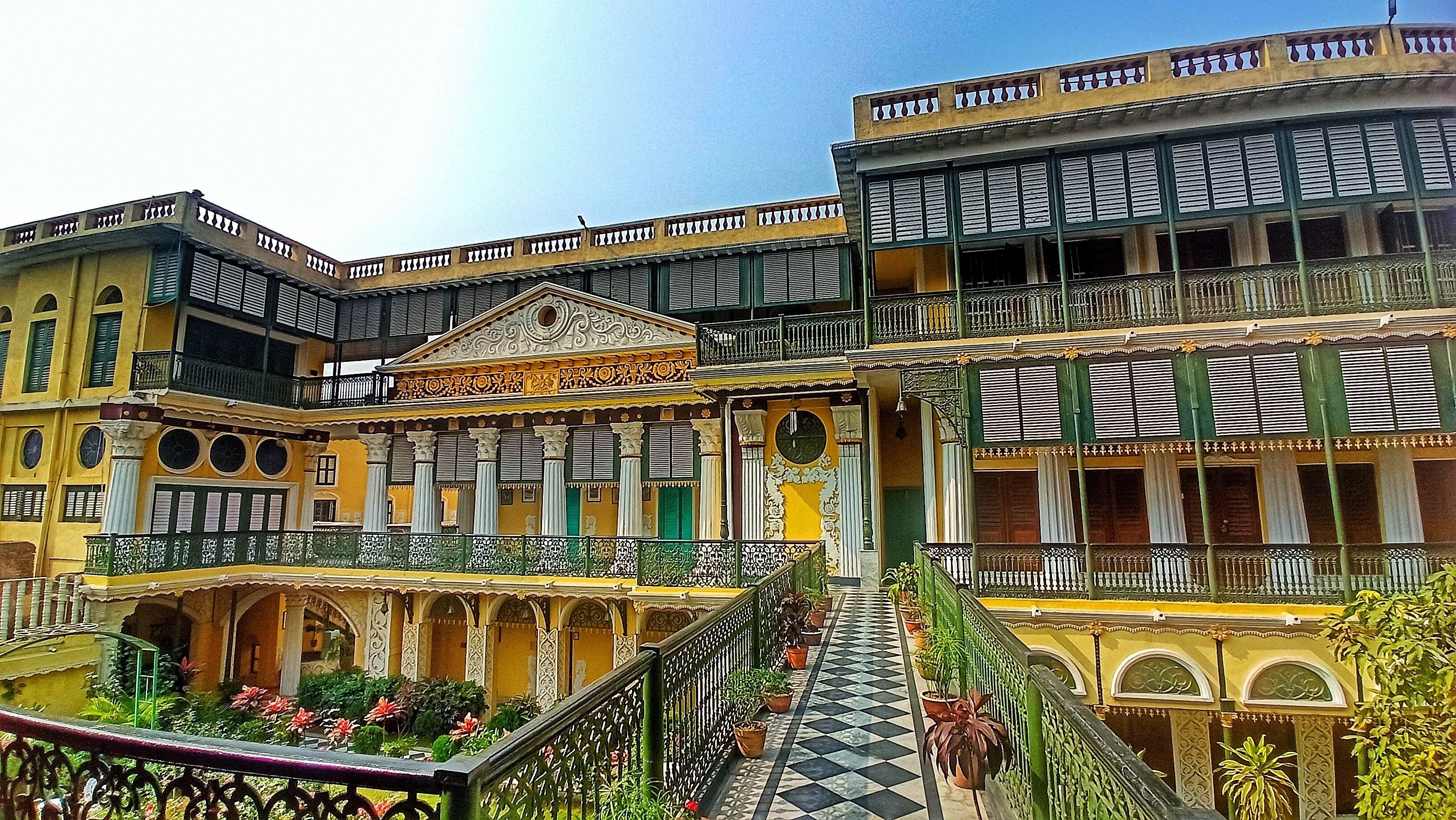 A multi-story building with balconies, a central courtyard with potted plants, and a checkered floor pattern.