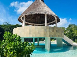Uma construção com telhado de palha e uma piscina logo abaixo.