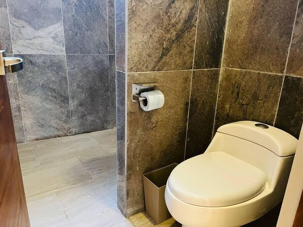 Um banheiro com vaso sanitário, lixeira e suporte para papel higiênico na parede.