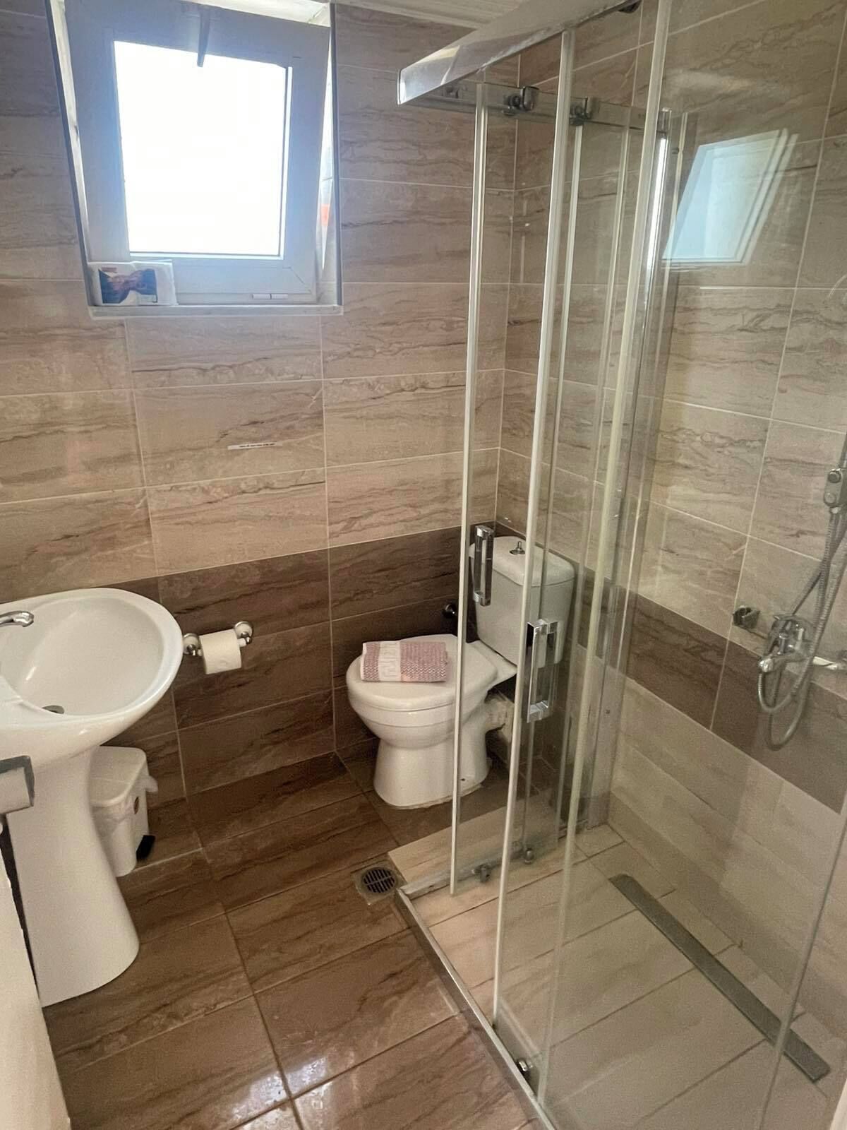 A bathroom with a glass-enclosed shower, a toilet, and a sink.