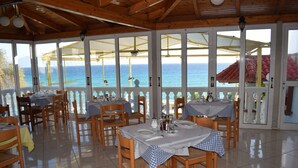 A restaurant with tables set for dining, large windows offering a view of the sea, and a wooden ceiling. - CLEAR HORIZON (Zakynthos)