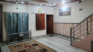 A spacious room with a marble floor, a patterned rug, a ceiling fan, a clock, and a staircase.