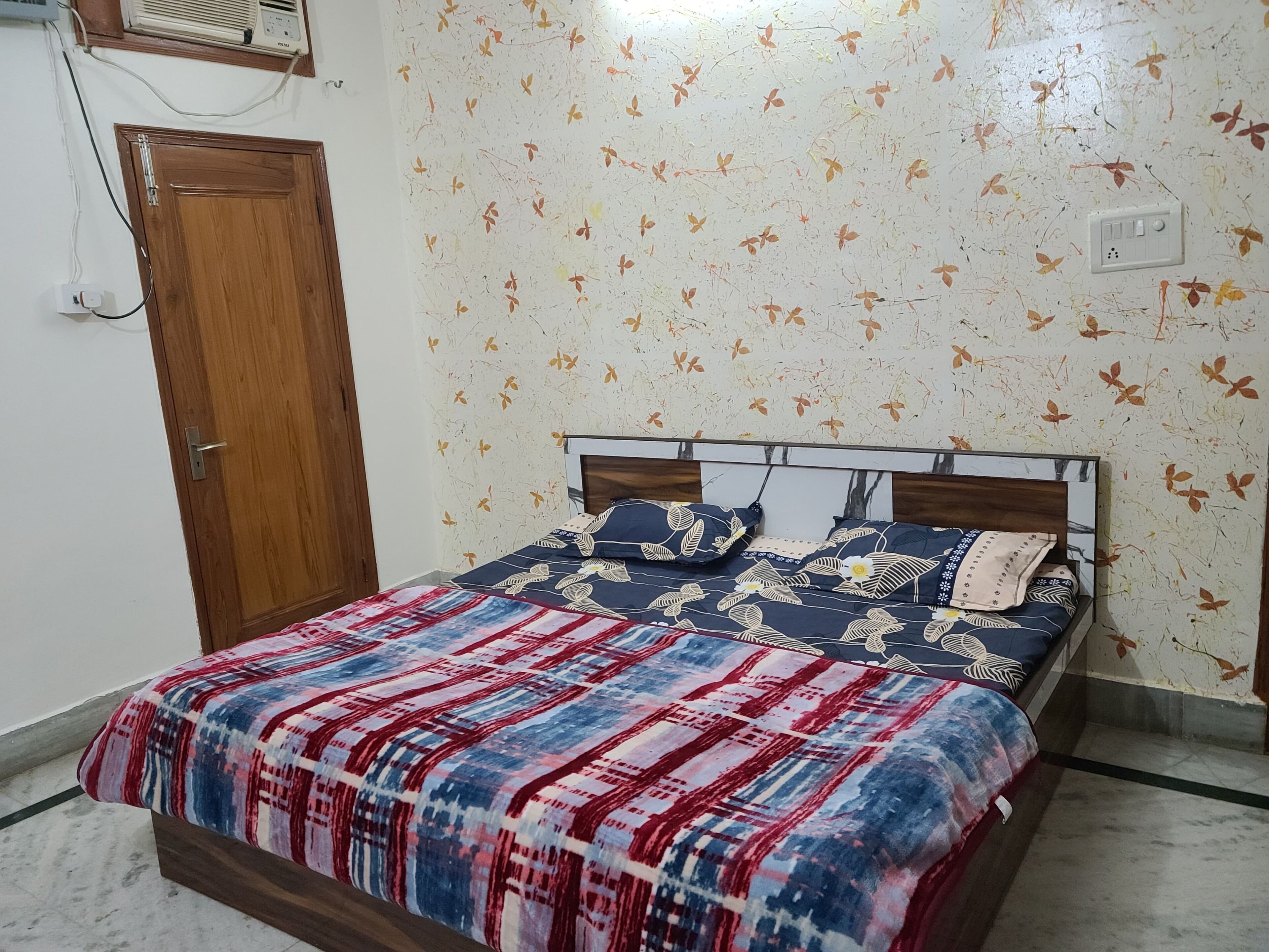 A bedroom with a bed, a wooden door, and a wall with a leaf pattern.